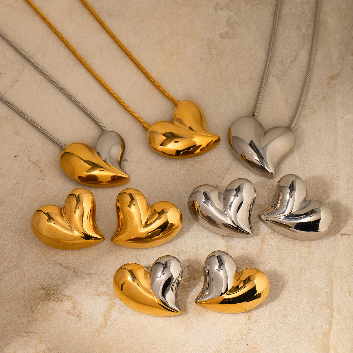 Flatlay of matching heart necklaces and earrings in gold and silver, styled on stone surface