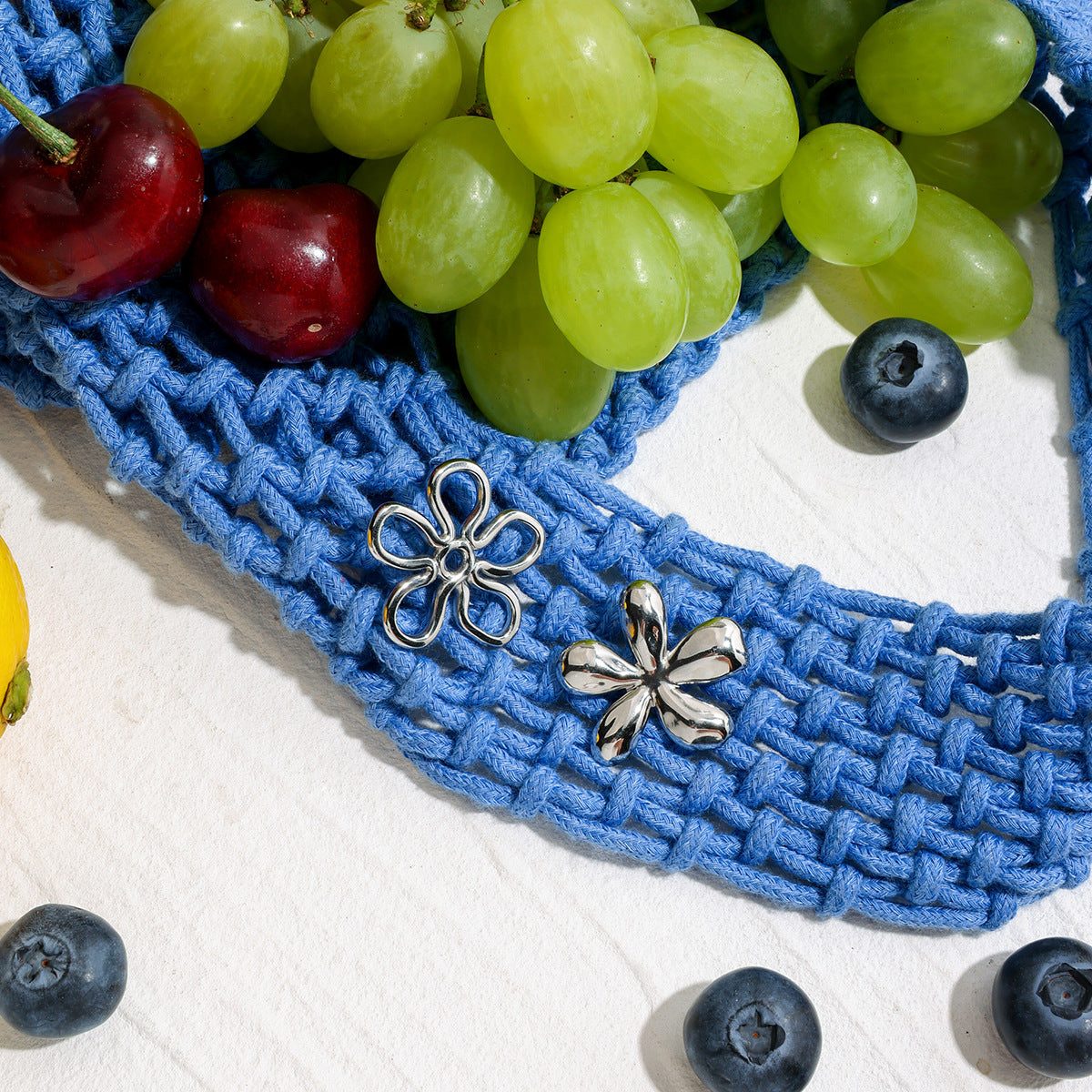 Hollow silver flower earrings styled with fruits on blue knit background
