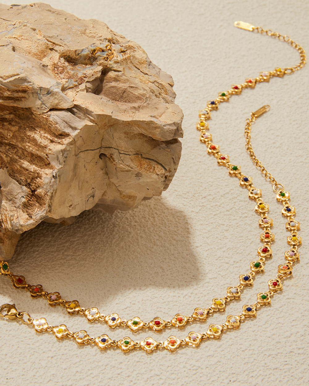 Gold necklace with colored beads on a textured beige surface