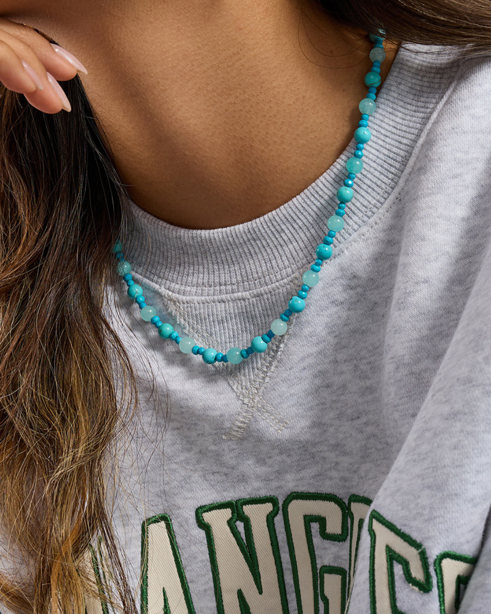 Person wearing a turquoise beaded necklace with a gray sweatshirt