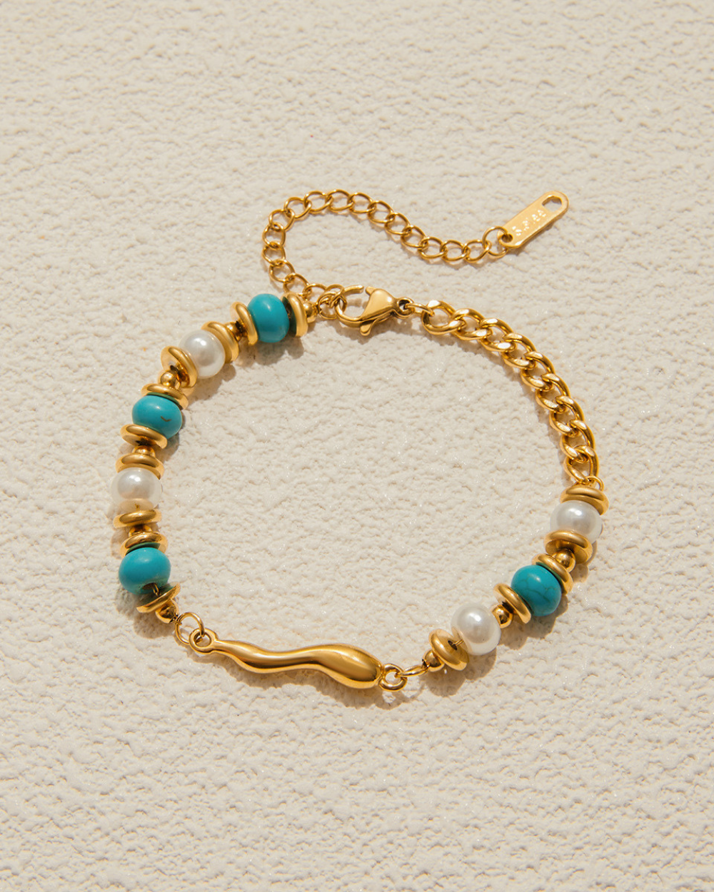 Gold bracelet with turquoise and pearl beads on a textured beige background