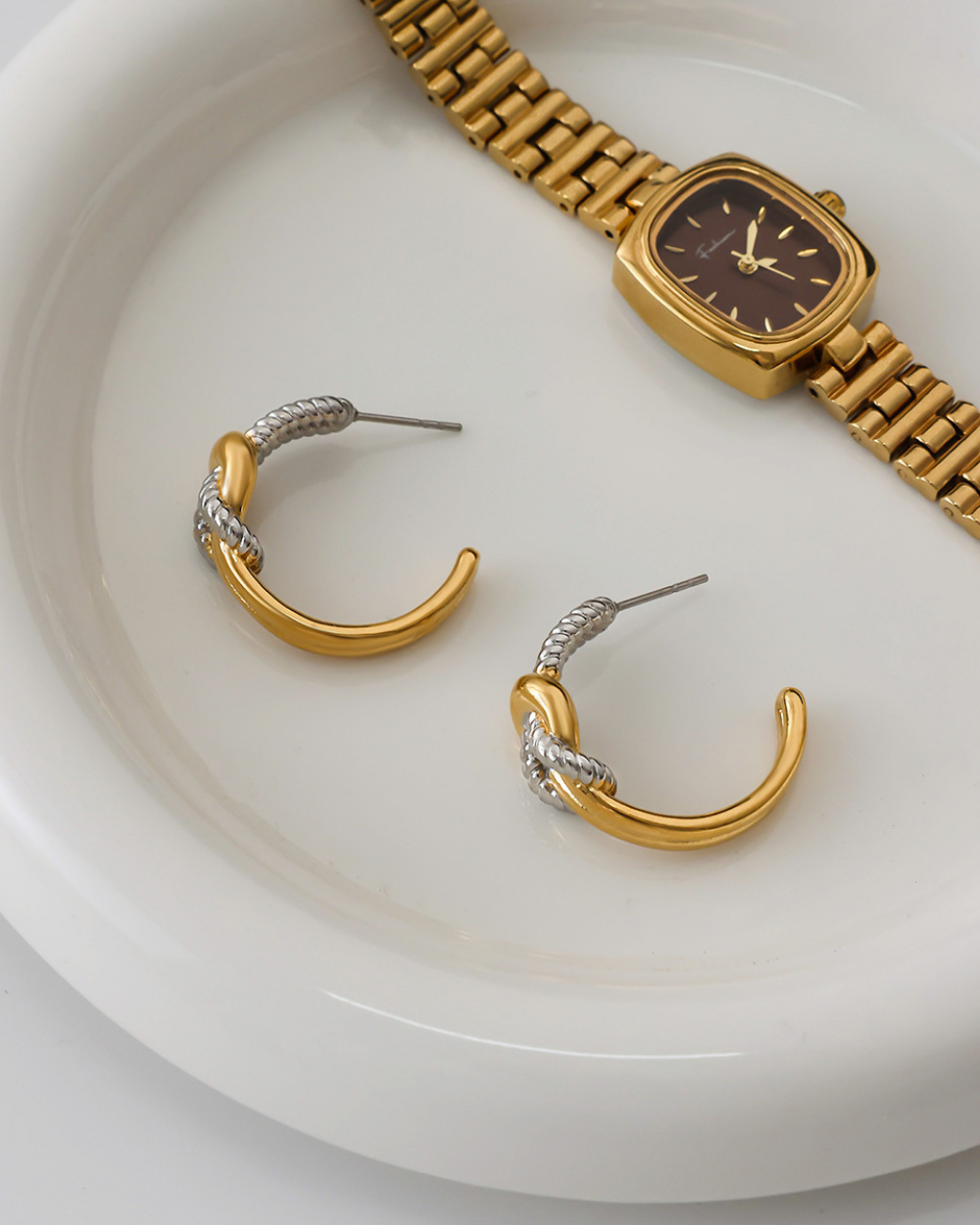 Gold hoop earrings and watch on a white plate