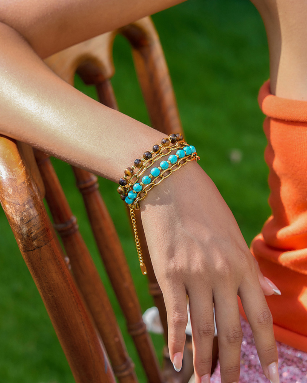 Hand wearing a gold bracelet with turquoise stones on a blurred green background