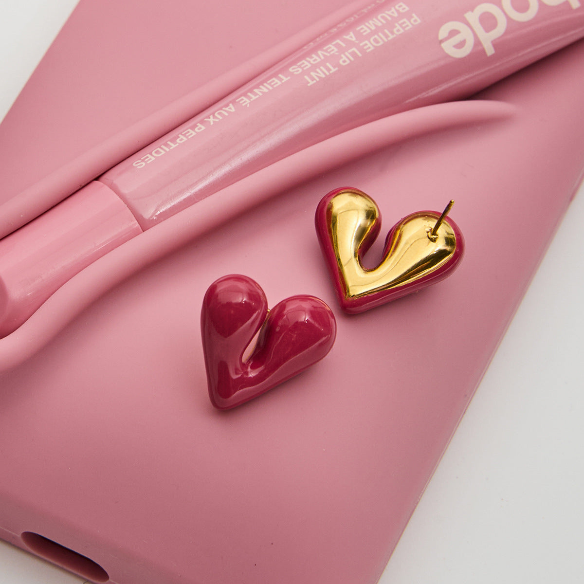 Red heart-shaped earrings next to pink accessories