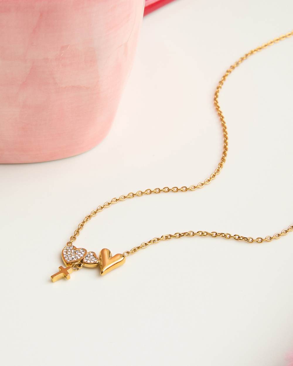 Gold necklace with heart and key pendant on a light pink background