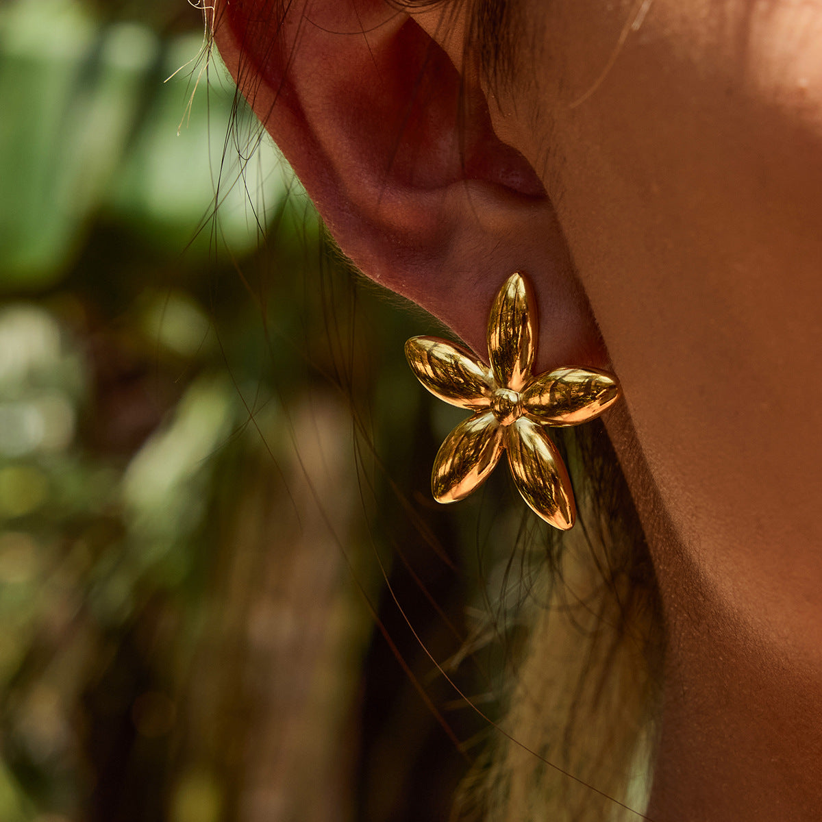 Model with slick hair wearing gold floral earrings in a tropical setting
