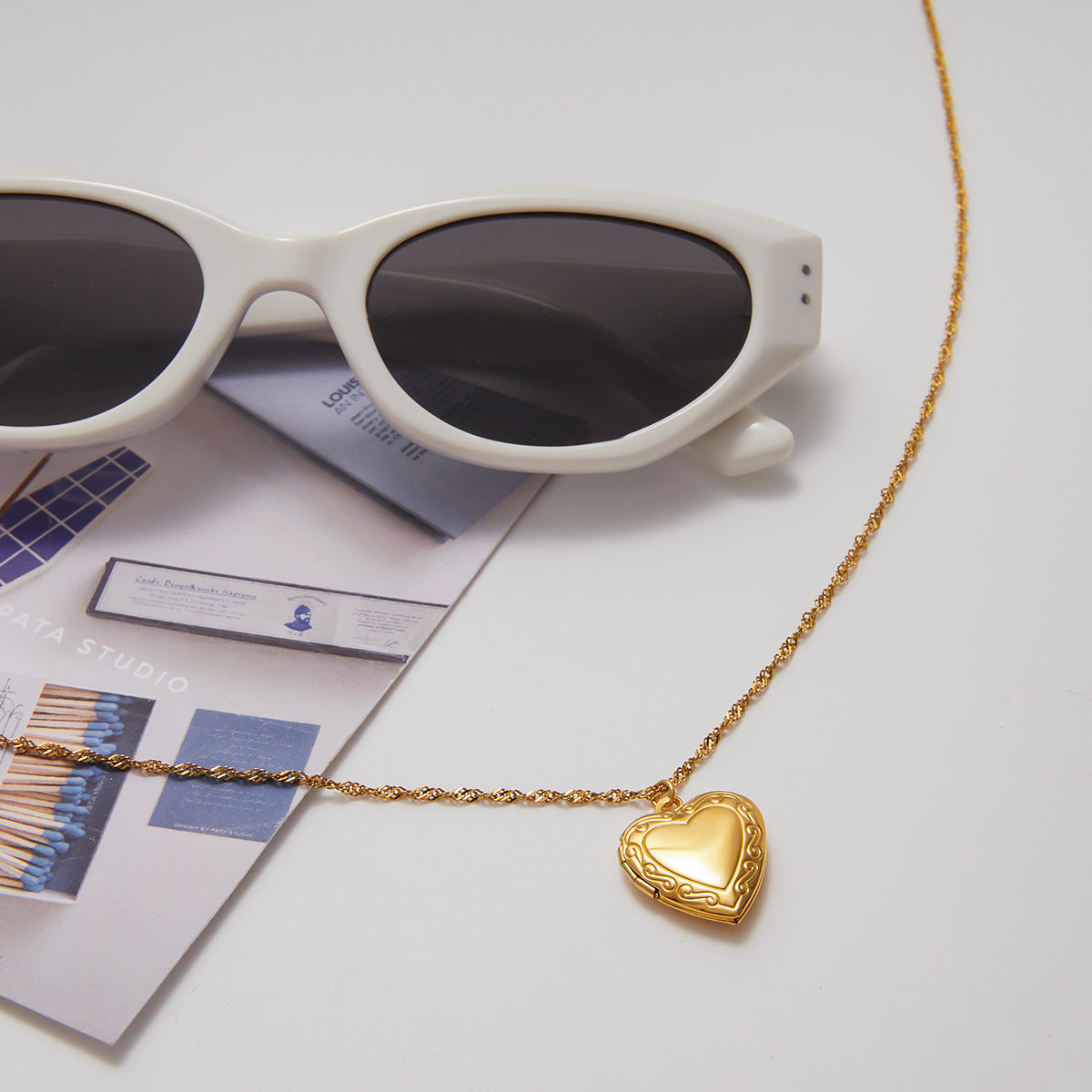 Gold heart-shaped necklace with sunglasses on a light surface