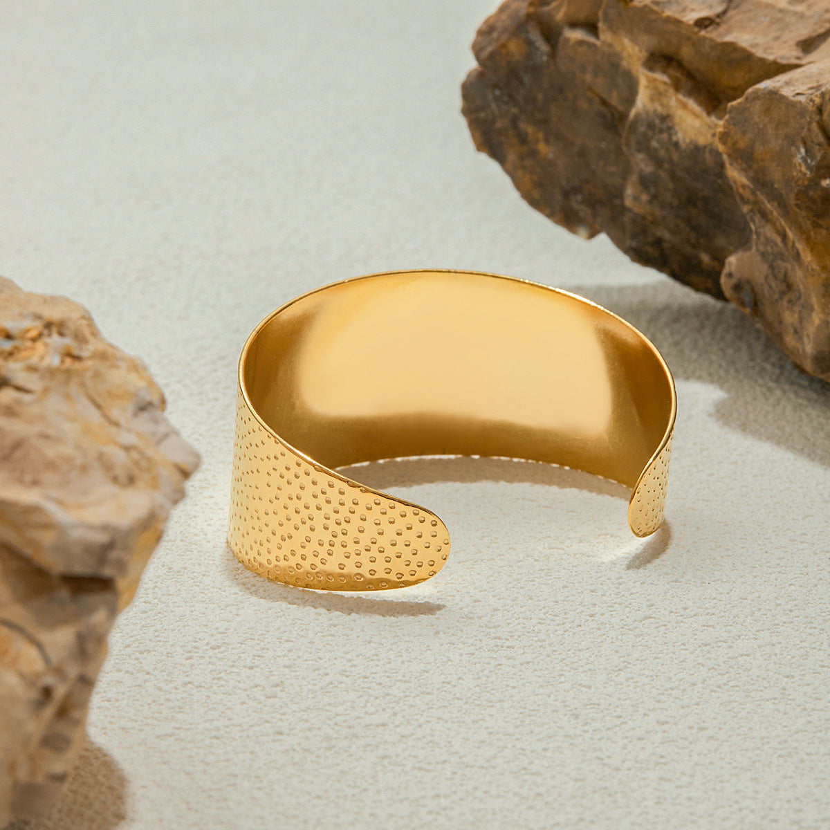 Gold bracelet with textured surface on a light gray background