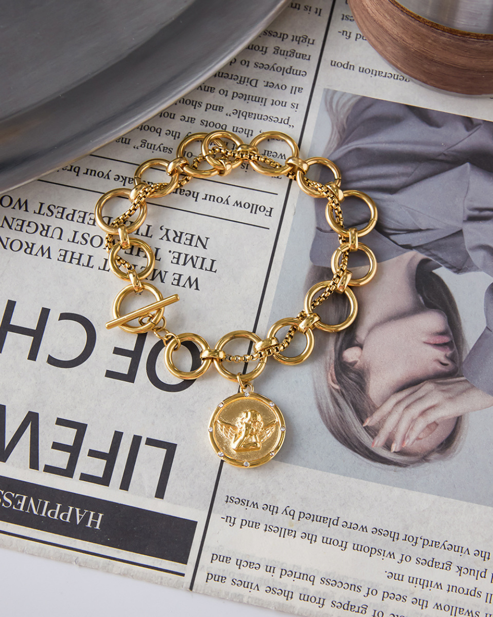 Gold chain bracelet with a coin charm on a newspaper background