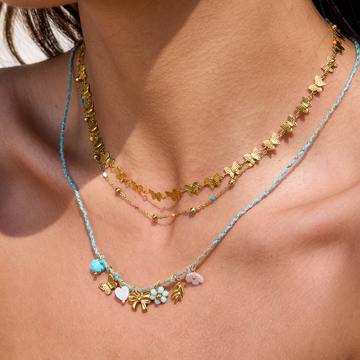 Model wearing layered bohemian necklaces including teal cord necklace with bow and floral charms