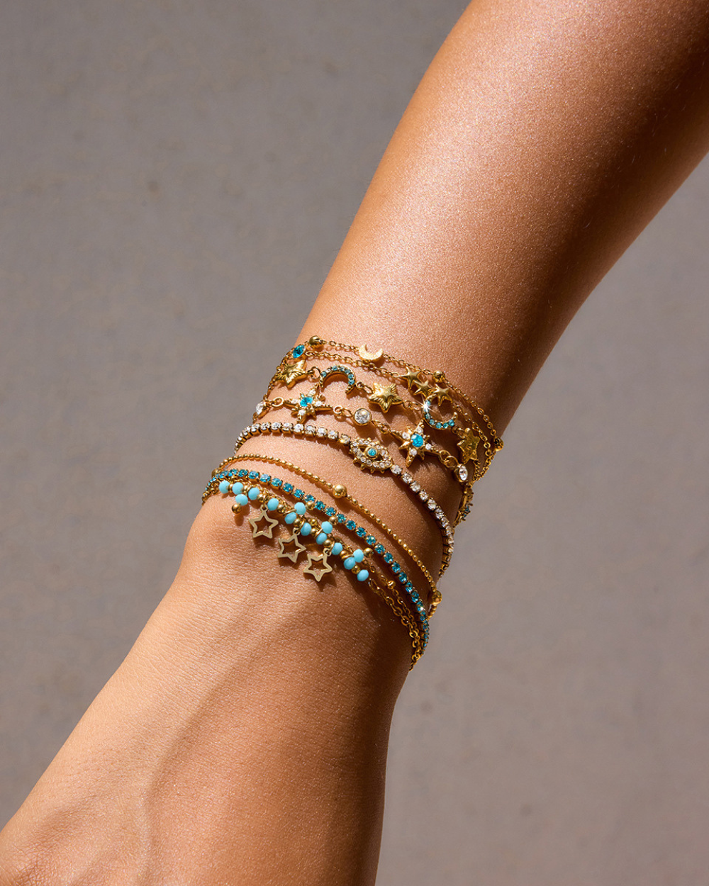 Multiple gold and turquoise bracelets on a wrist against a neutral background