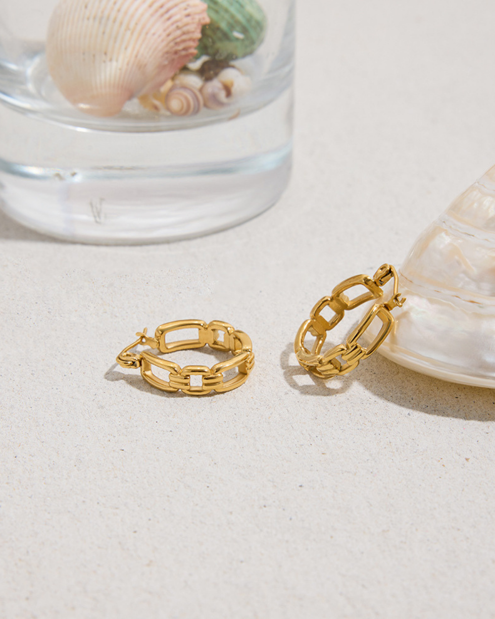 Two gold chain-link rings on a sandy surface with shells in the background.