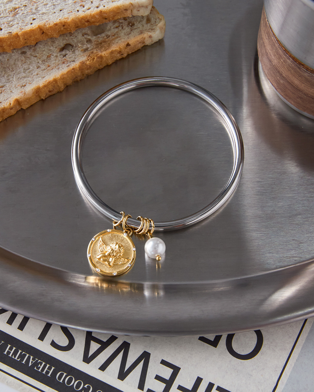 Silver bangle with gold coin and pearl charm on a metallic surface