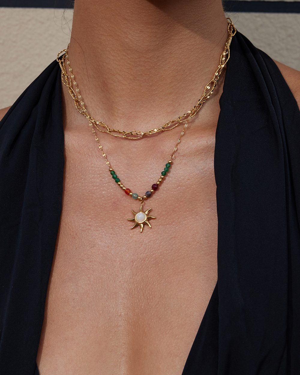 Gold necklace with a sun pendant and gemstones on a person wearing a black top.