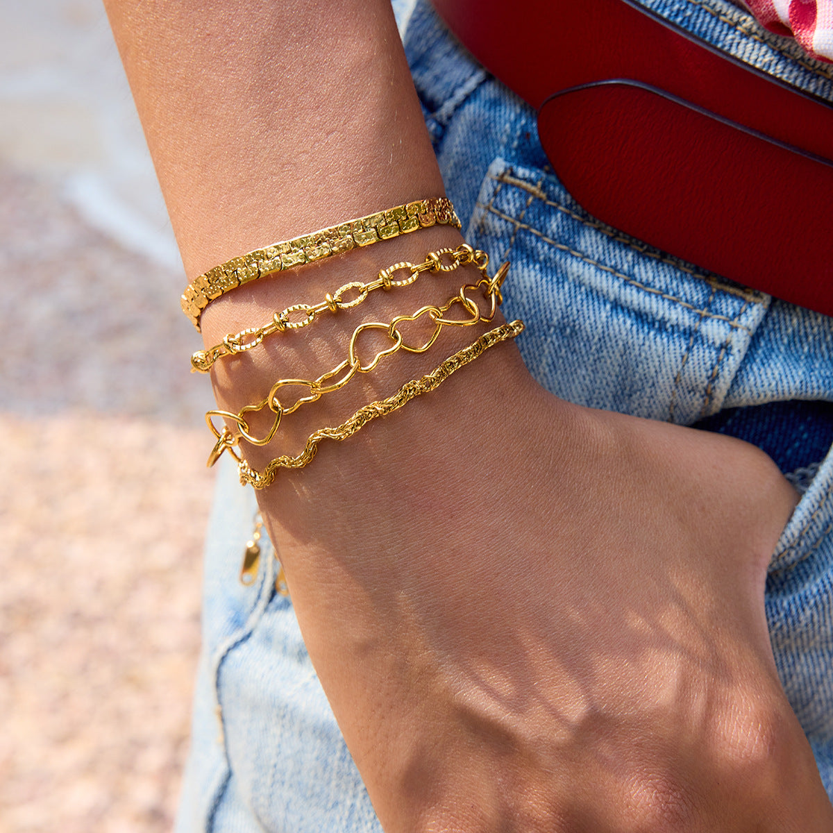 Stacked gold bracelets featuring heart-shaped chain design paired with textured bangles