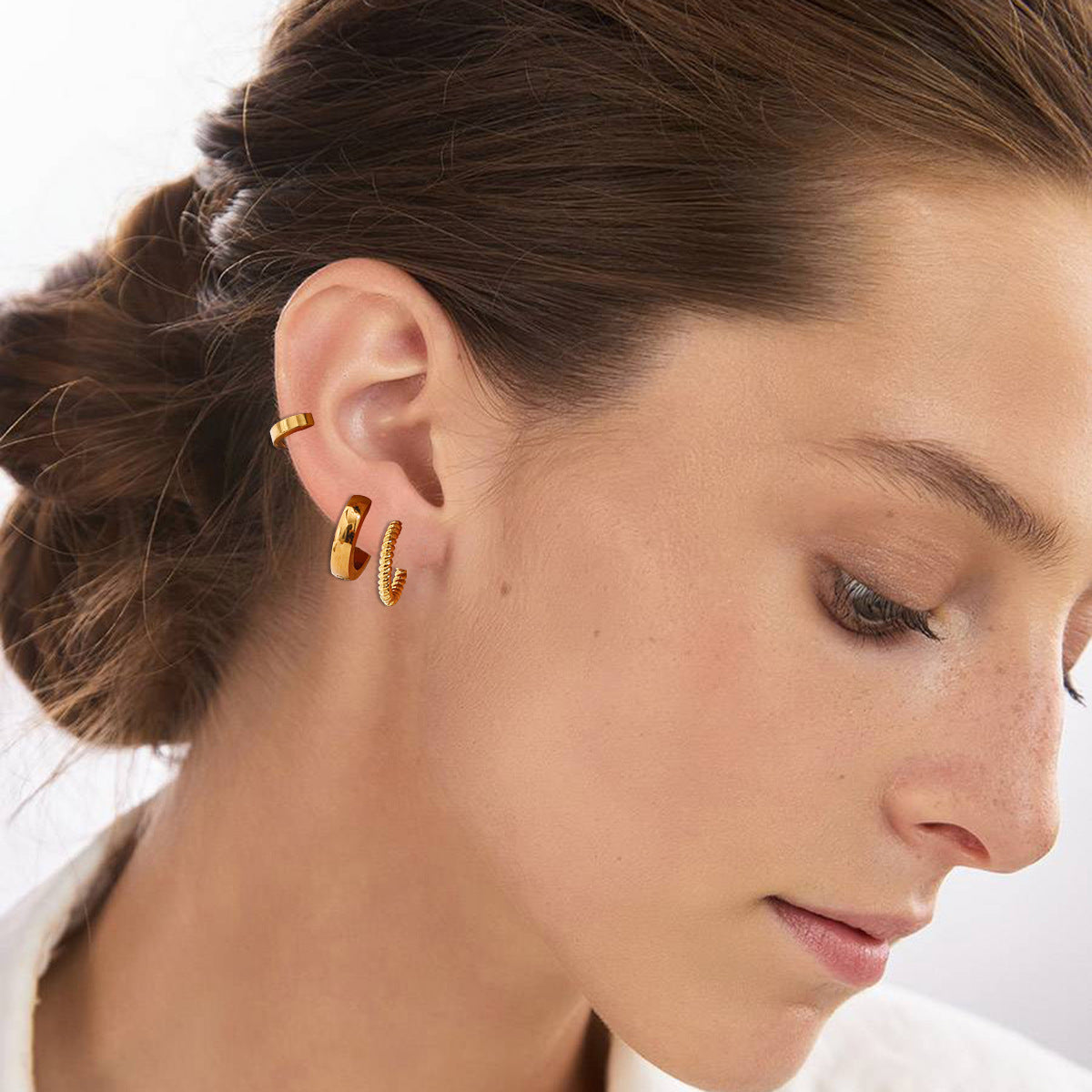 Model wearing stacked gold hoop earrings in different textures, styled with a bun