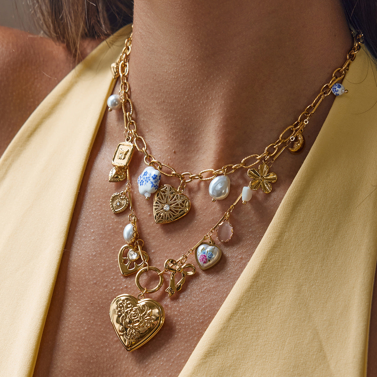 Model wearing layered vintage gold charm necklace set with heart locket and ceramic beads
