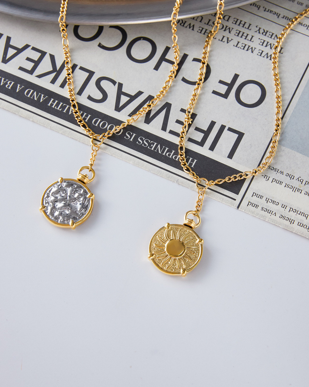 Two gold necklaces with pendants on a newspaper background