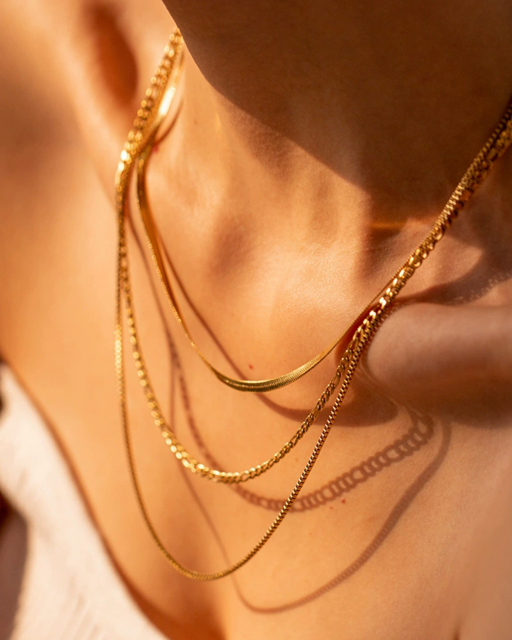 Close-up of a person wearing multiple gold necklaces on a blurred background