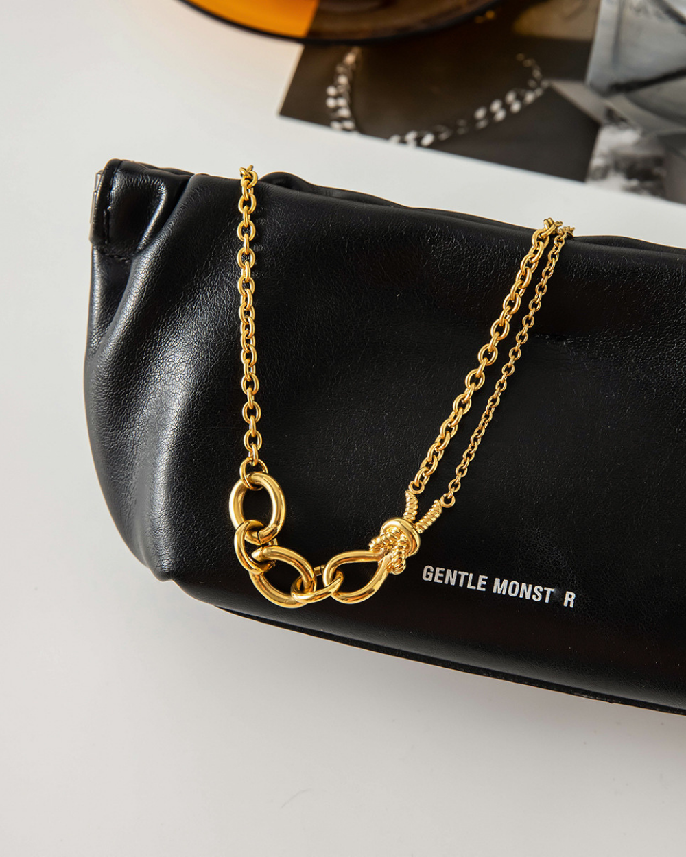 Gold chain necklace on a black handbag with 'GENTLE MONSTER' branding.