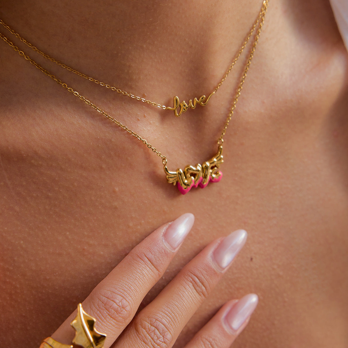 Model wearing layered gold love necklaces with glossy nails and pearl ring