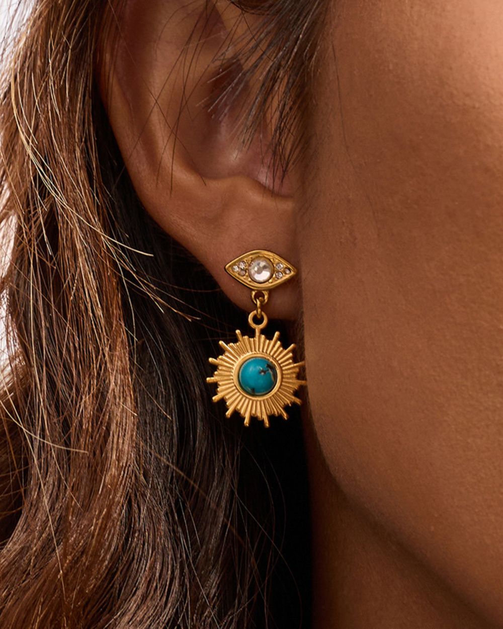 Close-up of a gold earring with a turquoise stone worn by a person.