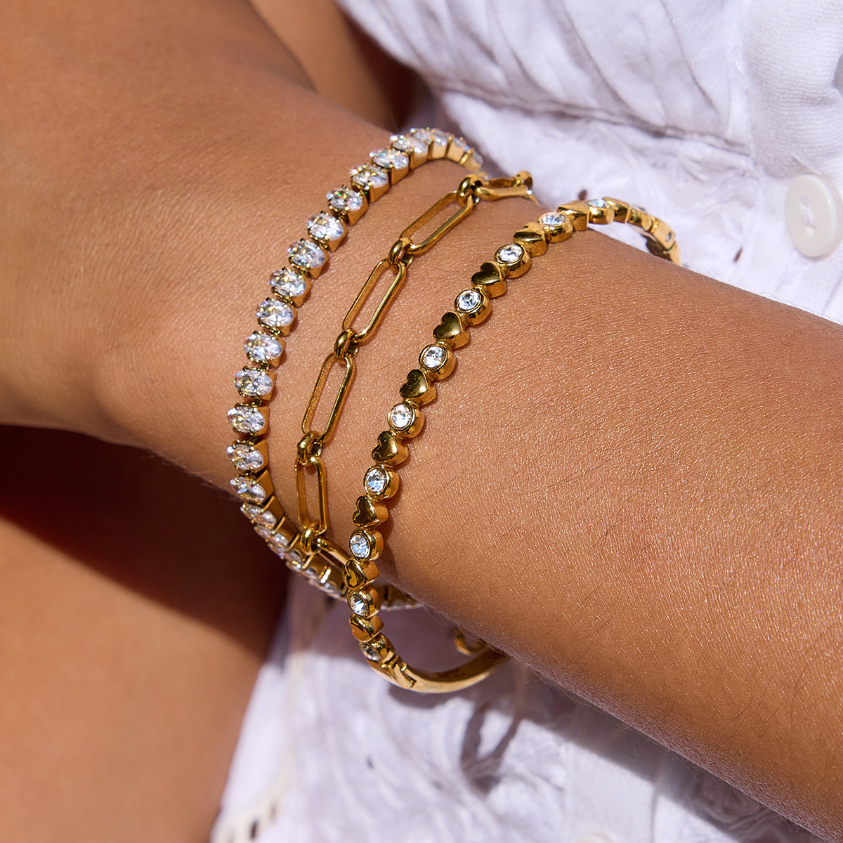 Close-up of model wearing sparkling tennis bracelet and gold heart chain in sunlight