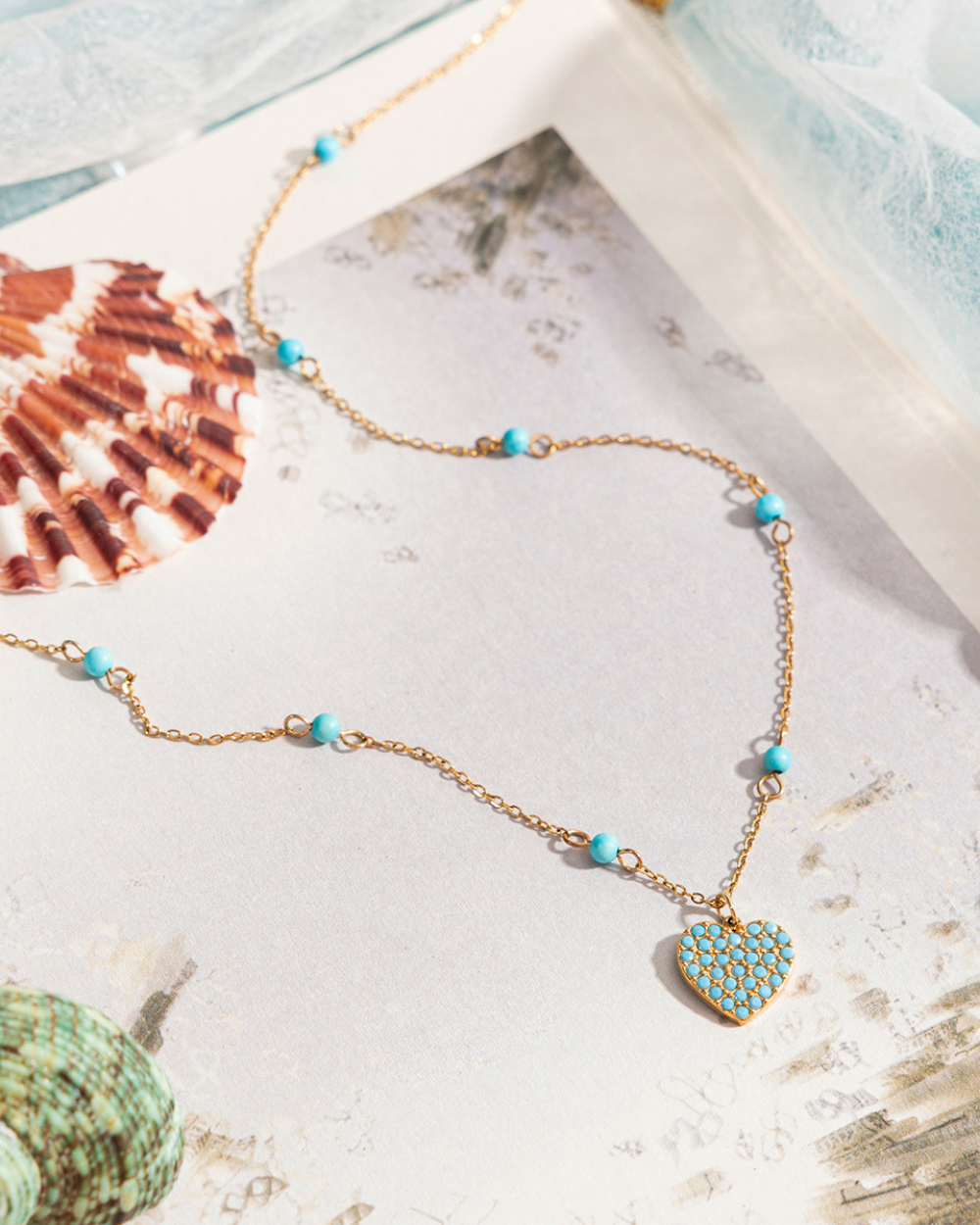 Necklace with heart pendant and turquoise beads on a textured surface with shells.
