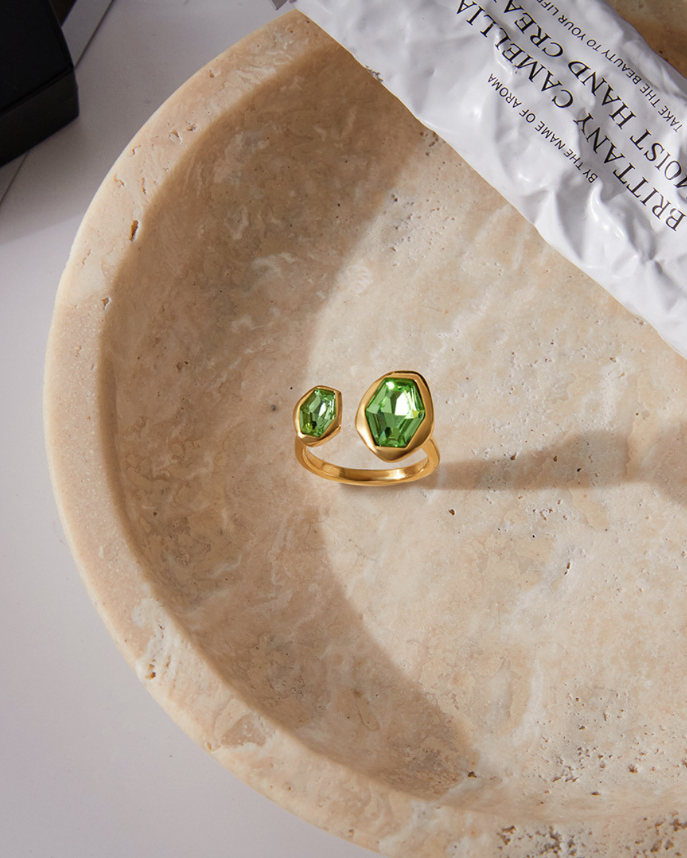 Gold ring with green gemstones on a beige stone surface