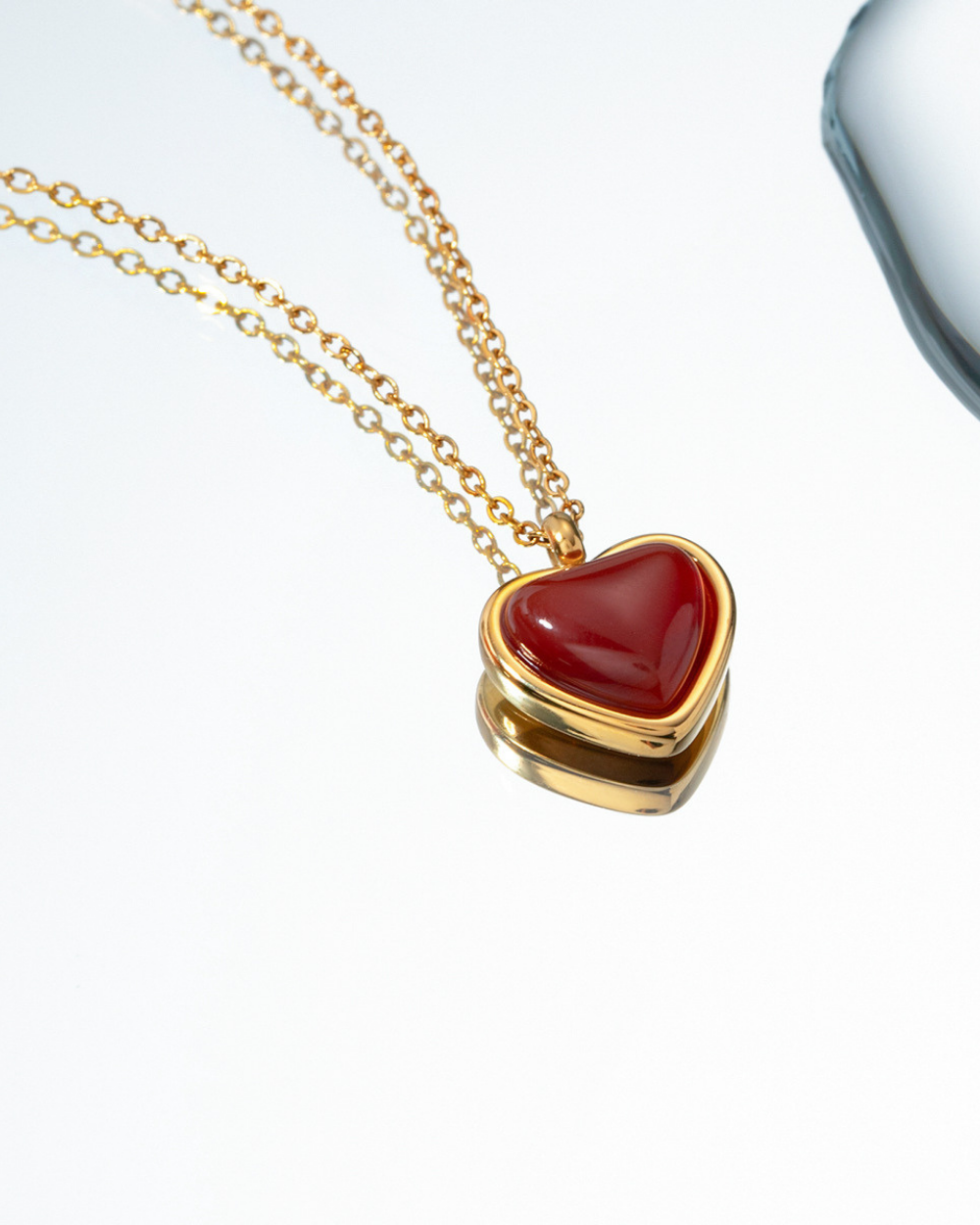 Gold necklace with a red heart pendant on a white background