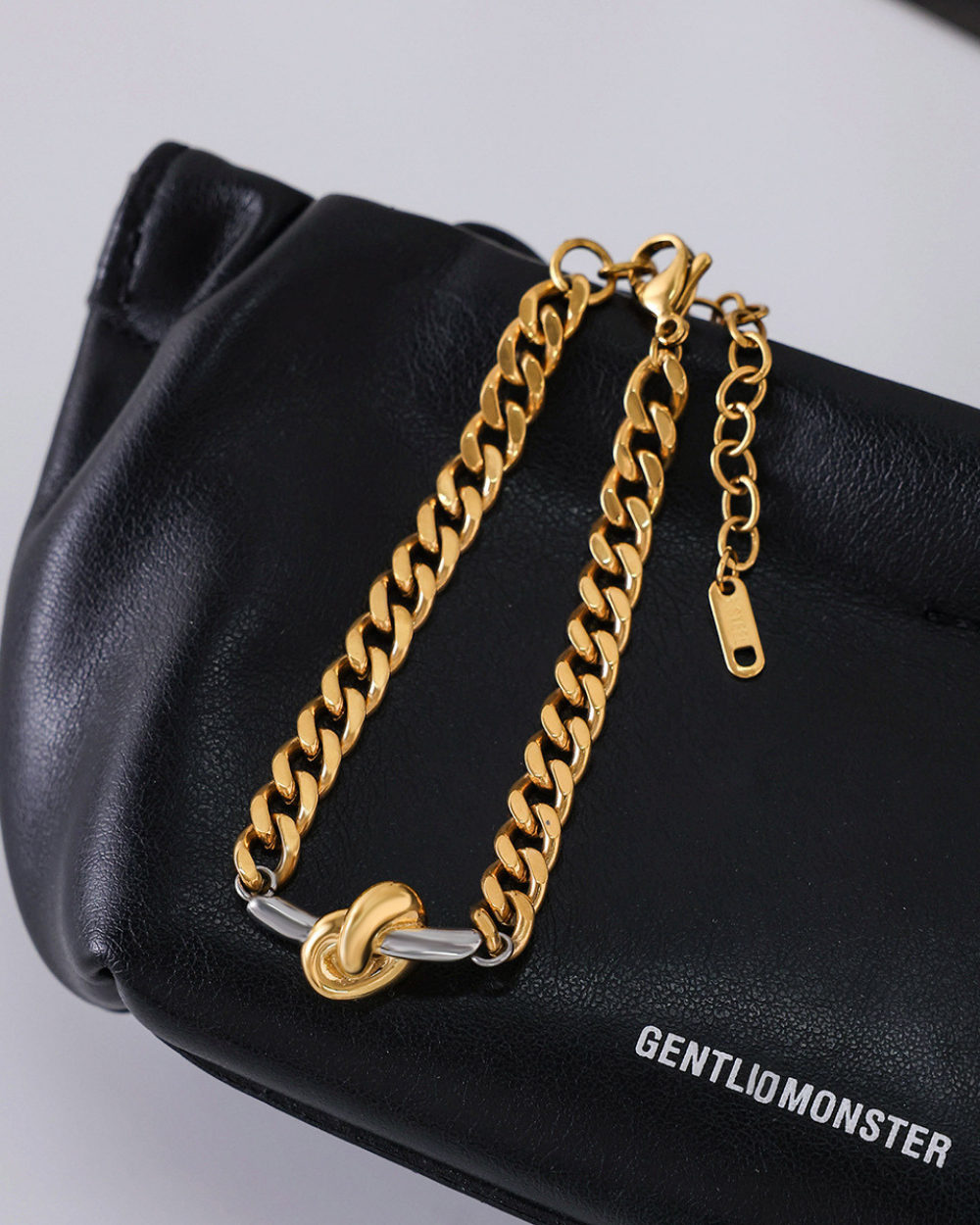 Gold chain bracelet on a black handbag with 'GENTLIOMONSTER' branding.