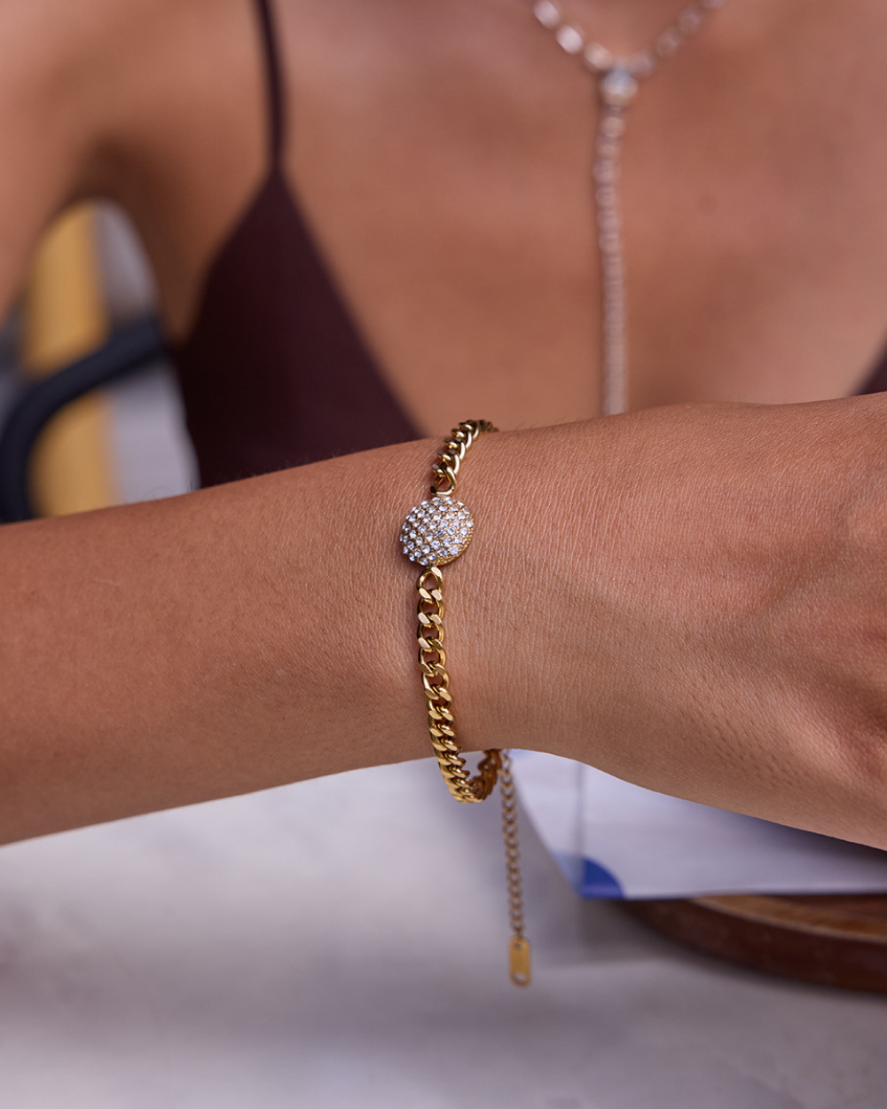 Gold bracelet with a diamond charm on a wrist against a blurred background