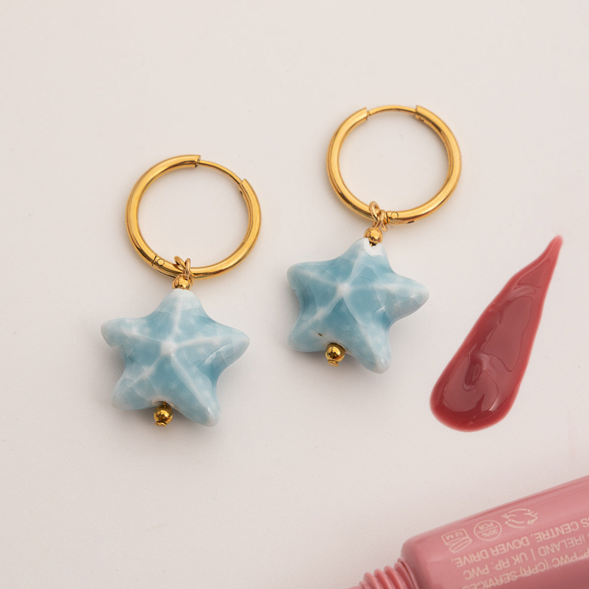 Gold hoop earrings with star-shaped blue charms on a light pink background