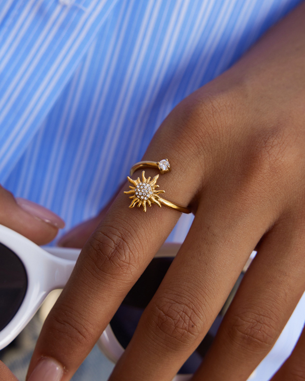 Gold sun-shaped ring on a finger with a blue background