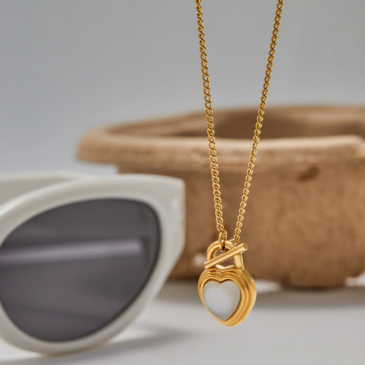 Gold heart pearl pendant necklace styled next to sunglasses and accessories