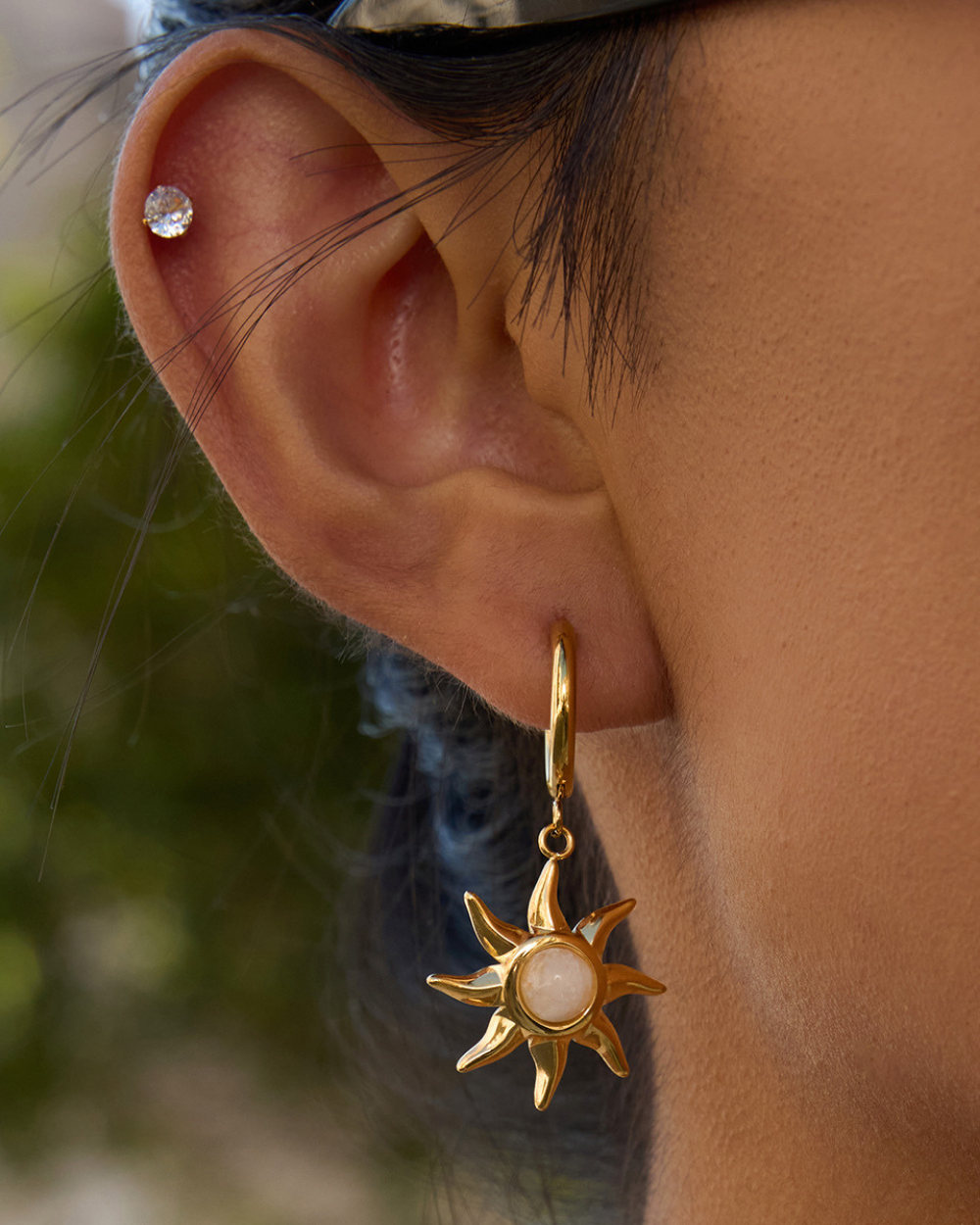 Close-up of an ear wearing a gold sun-shaped earring with a central gemstone.