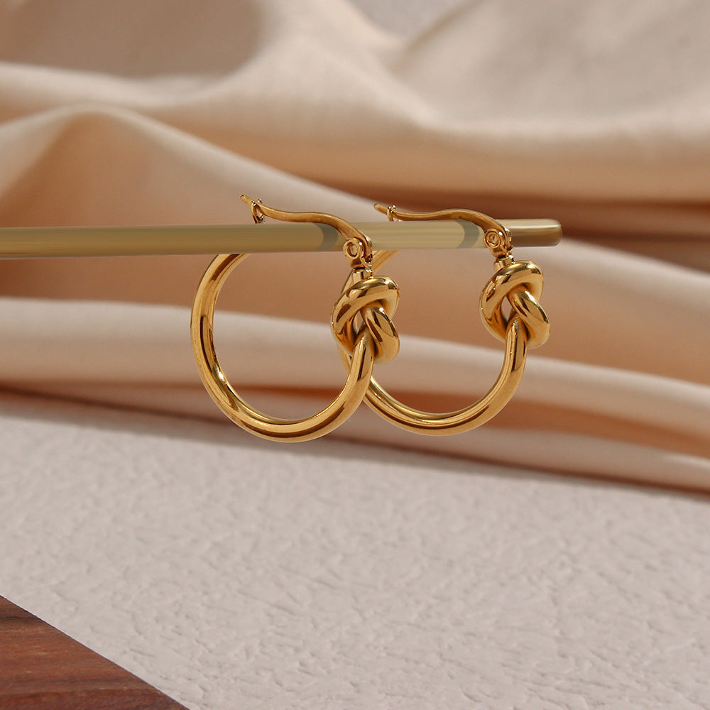 Ear detail showcasing knotted hoop earrings paired with small stud