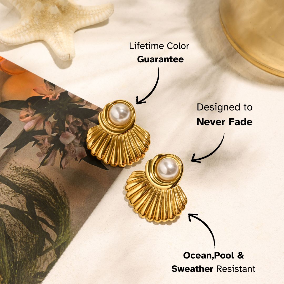 Gold scallop shell earrings with pearls placed beside a starfish and floral book