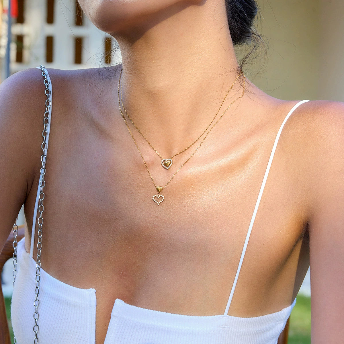 Close-up of a person wearing a gold necklace with heart pendants outdoors.