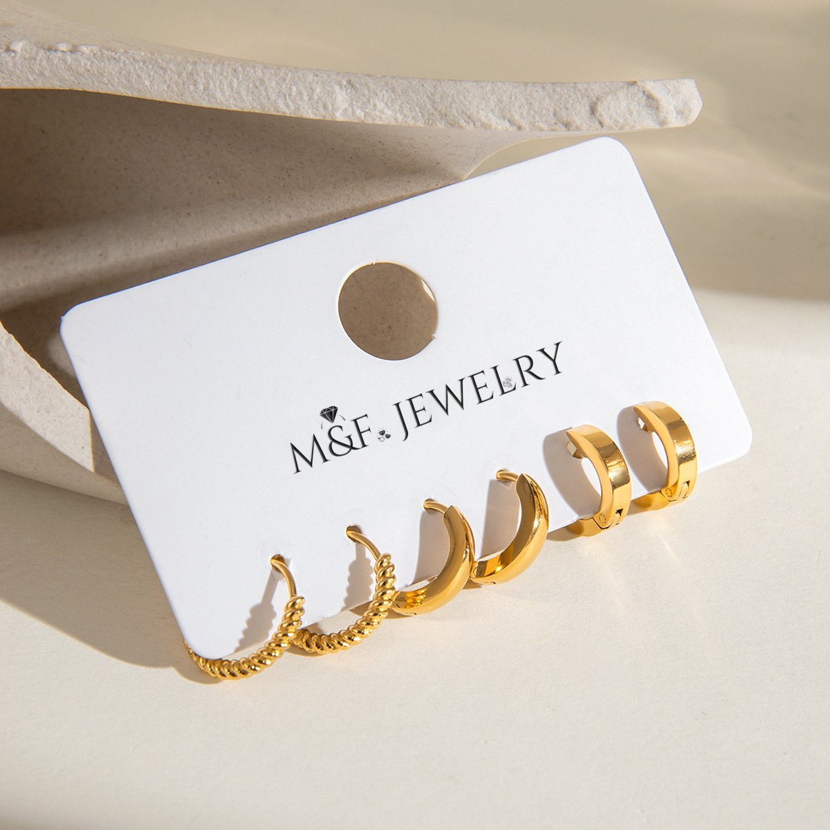 Sleek chunky gold hoop earrings placed on a display card under sunlight
