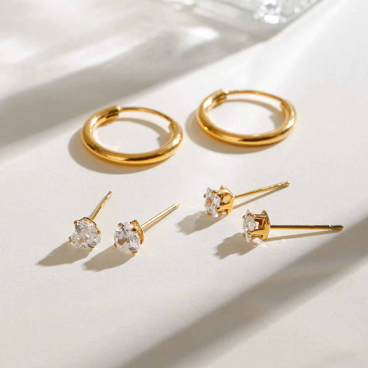 Minimalist flatlay of gold hoops and two styles of crystal stud earrings in bright natural light