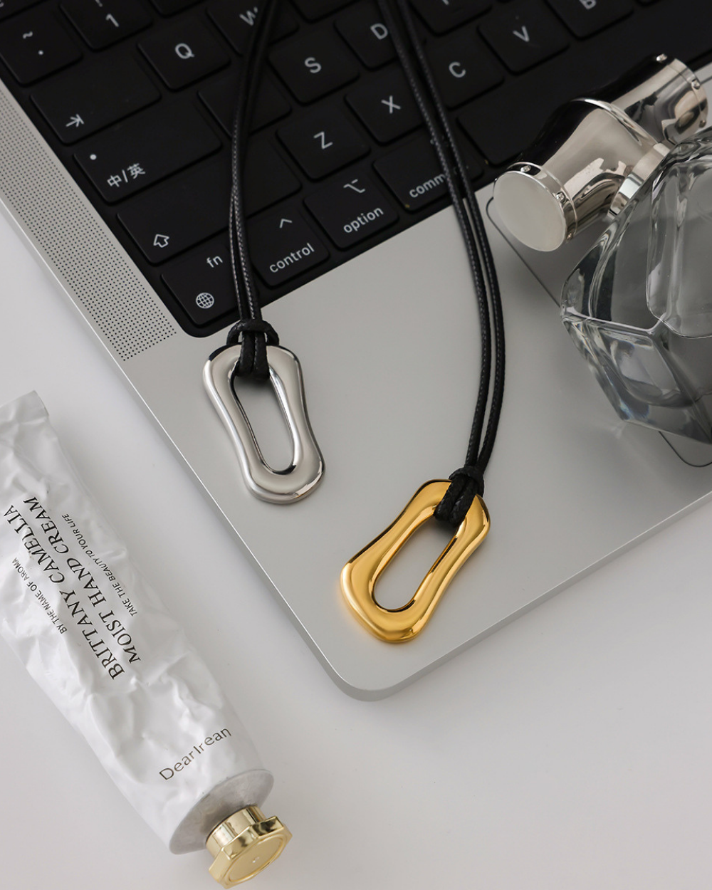 Two keychains, one gold and one silver, on a laptop keyboard with a bottle and tissue paper in the background.