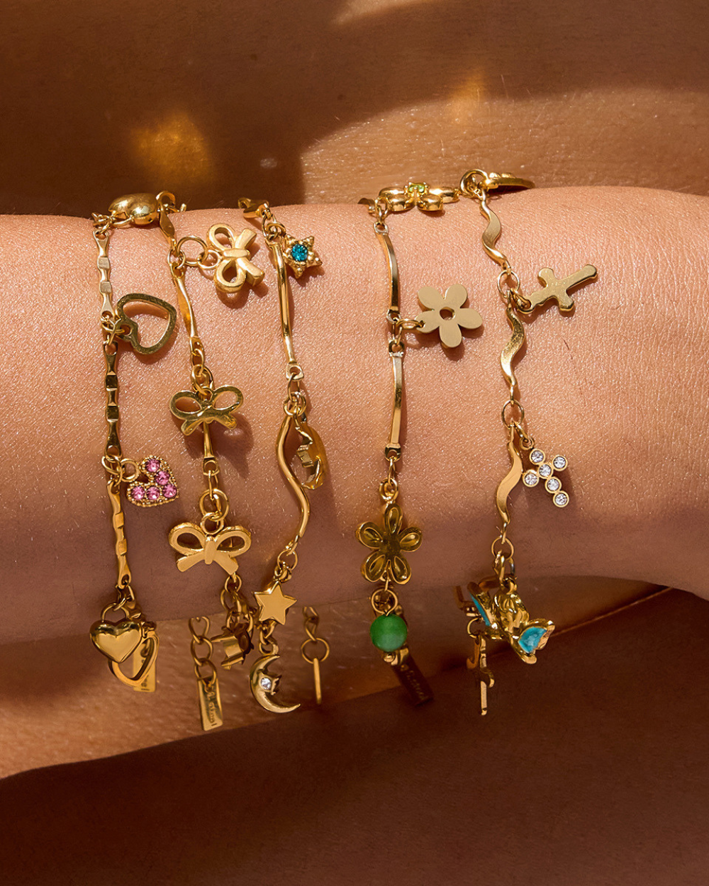 Gold bracelets with various charms on a wrist against a brown background