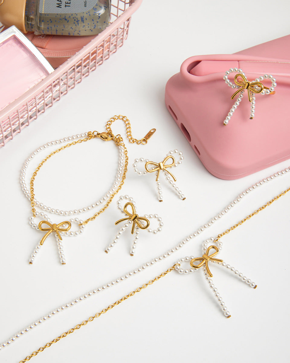 Gold and white bow-shaped jewelry on a light surface with a pink case in the background.