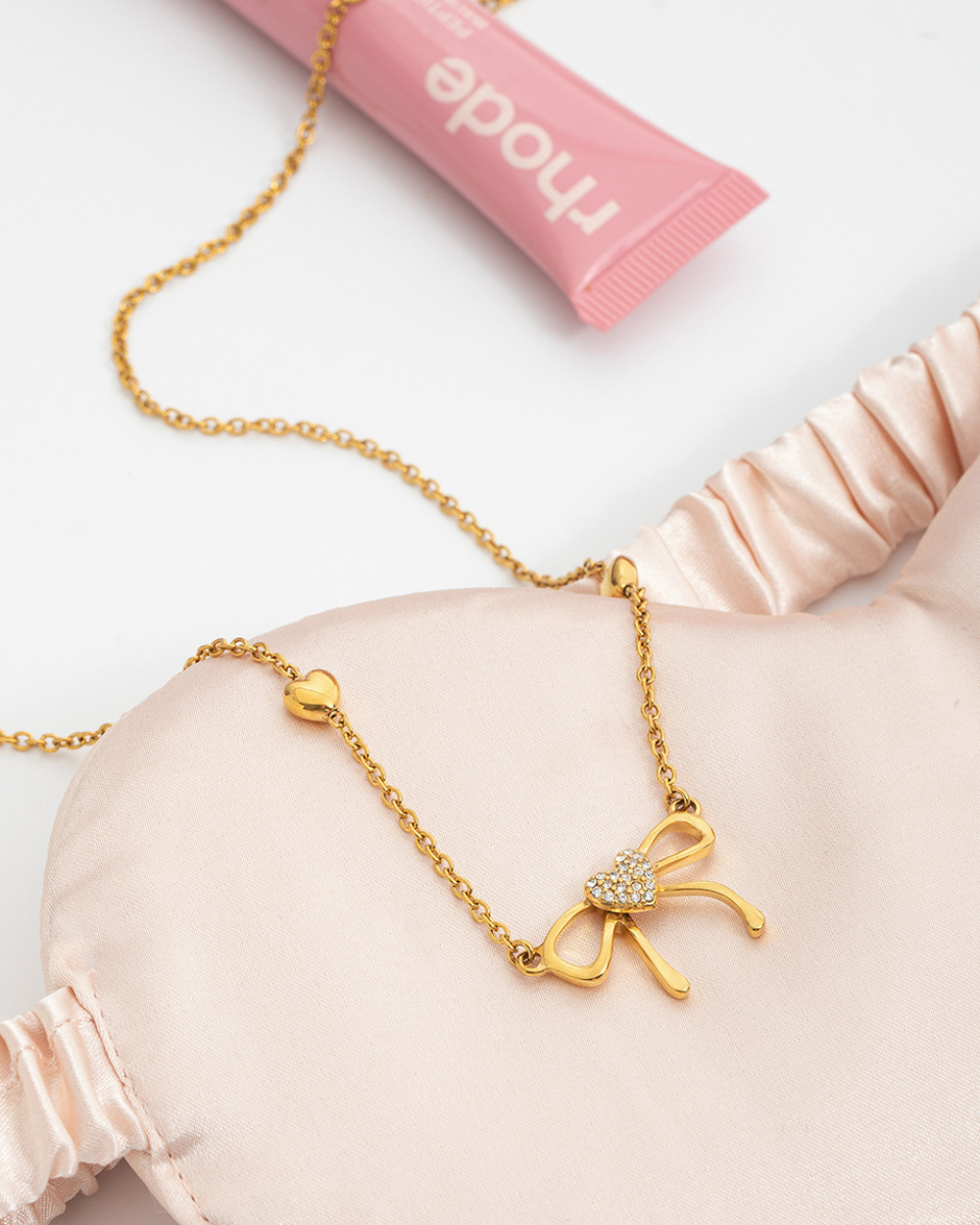 Gold bow-shaped necklace on a pink satin pillow with 'muse' branding in the background.