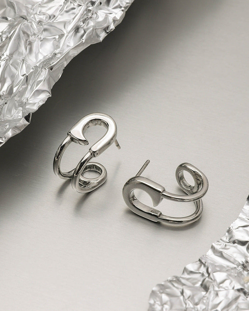 Silver hoop earrings styled on crinkled foil, showing bold contours and polished shine