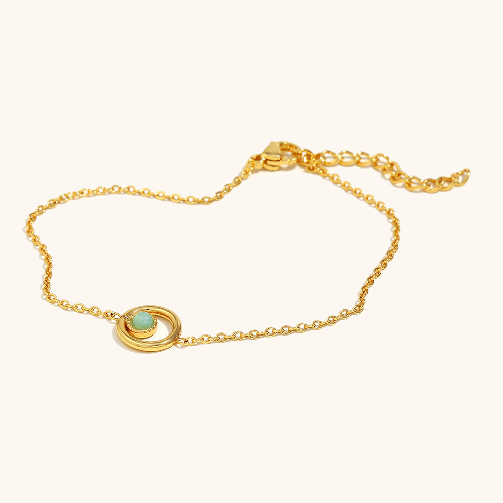 Close-up of dainty gold bracelet featuring a round green bead in orbit-style setting.