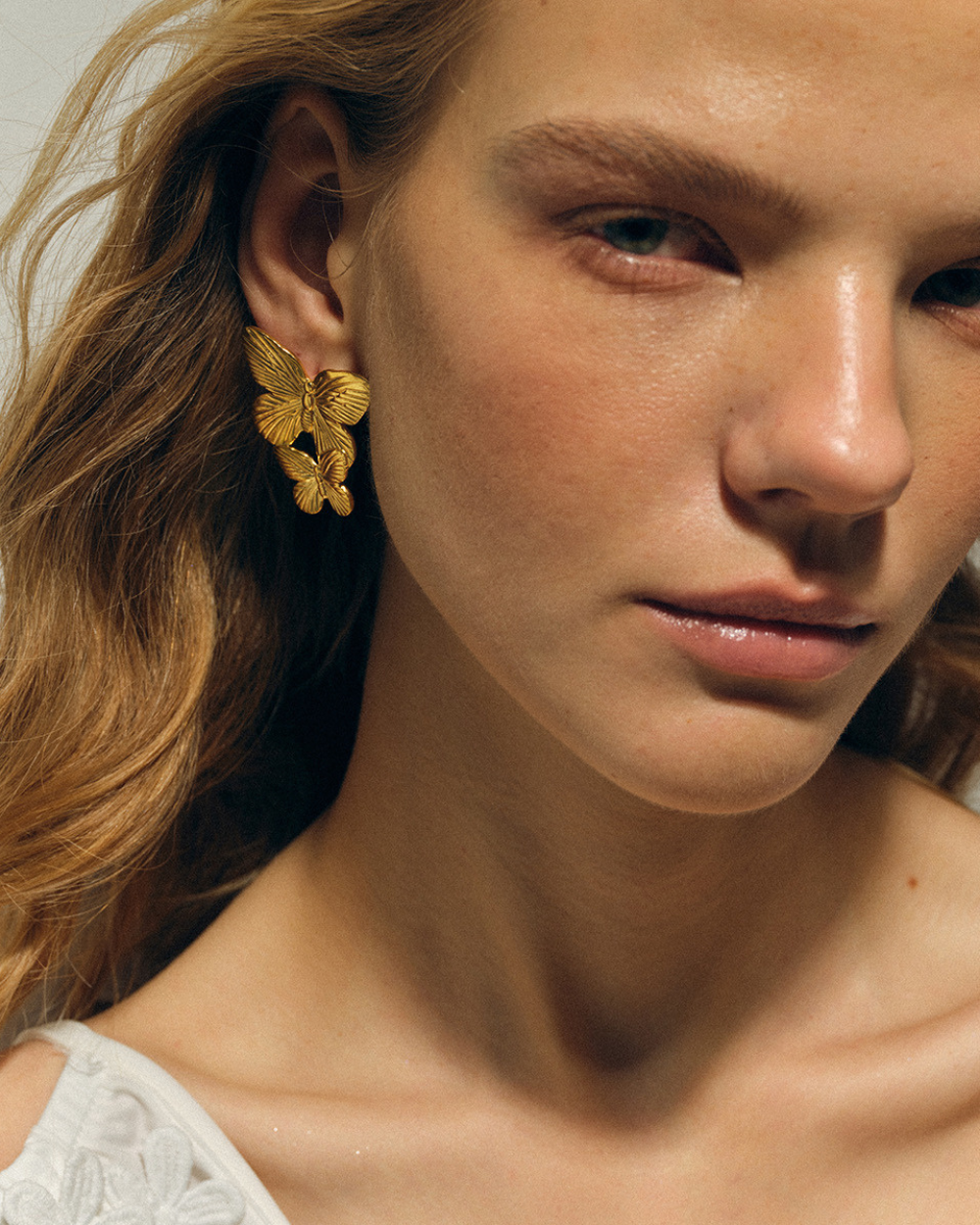 Close-up of a woman wearing gold butterfly earrings with a neutral background