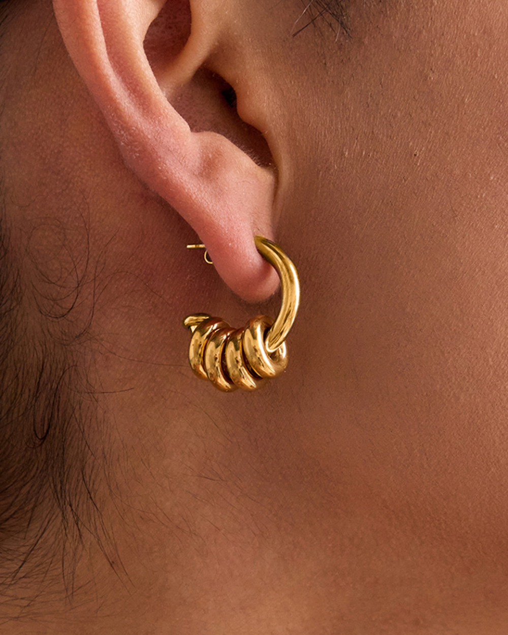 Gold hoop earring worn on an ear with a close-up view