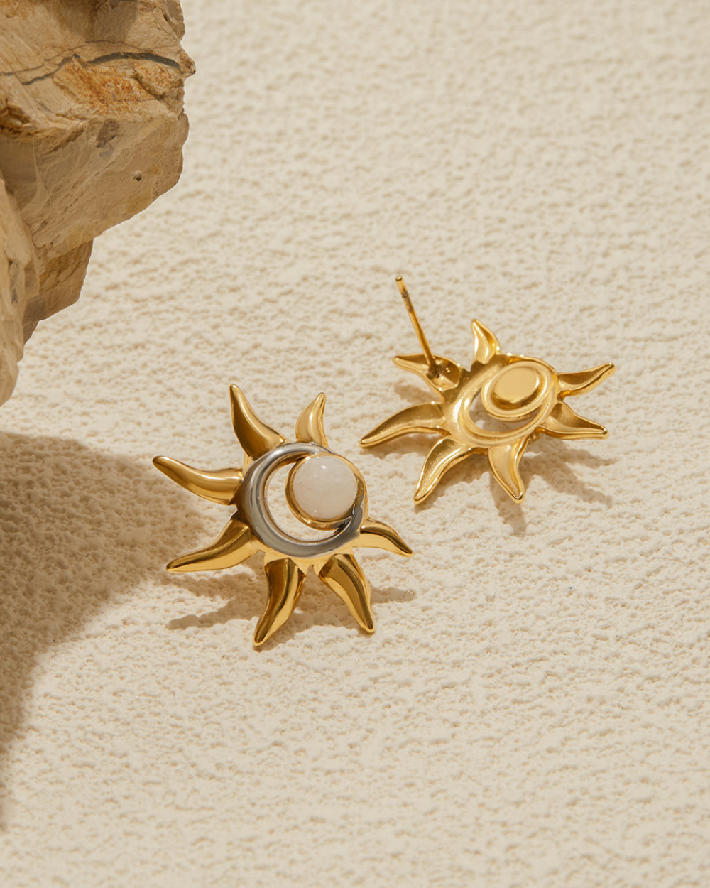 Gold sun-shaped earrings with a central moon on a beige textured background